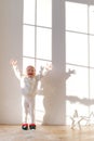 Vertical shot of overjoyed small girl dressed in white sweater and leggins, wears elf s shoes, plays with artificial