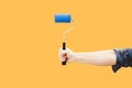 Vertical shot of a paint roller in the hand of a man, in a yellow background Royalty Free Stock Photo