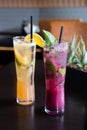 Vertical shot of a pair of colorful cocktails with leaves and straws on a wooden table