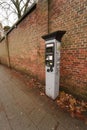 Vertical shot of a parking meter on a street before a red brick wall in a town Royalty Free Stock Photo