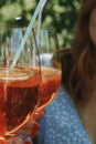 Vertical shot of people holding two glasses of aperol spritz with straws outdoors