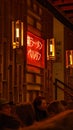 Vertical shot of people sitting under the Japanese neon lettering in a Ramen Restaurant in Kreuzberg