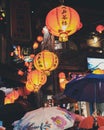 Vertical shot of people walking around with umbrellas under paper lanterns at night time