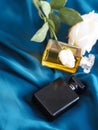 Vertical shot of perfumes bottles and white roses on a blue fabric surface