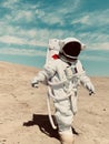 Vertical shot of a person in an astronaut spacesuit walking on the sandy surface under the blue sky