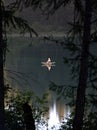 Vertical shot of a person canoeing a tranquil lake surrounded by green trees