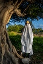 Vertical shot of a person covered by a white sheet, with sunglasses and hat,in appearance of a ghost