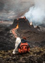 Vertical shot of a person with a dog looking at an active volcano with flowing lava