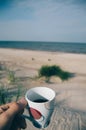 Vertical shot of a person holding a mug with coffee on a background of a beach Royalty Free Stock Photo