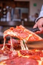 Vertical shot of a person holding a slice of pizza with a black tool Royalty Free Stock Photo