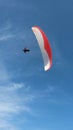Vertical shot of a person paragliding in a free fly with blue sky in the background