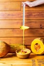 Vertical shot of a person pouring pumpkin soup in a bowl on a rustic background Royalty Free Stock Photo