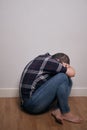 Vertical shot of a person sitting on the ground against a wall with head tucket arms and knees Royalty Free Stock Photo