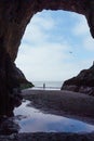 Vertical shot of a person standing at the entrance of a cave looking at the ocean Royalty Free Stock Photo