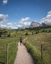 Vertical shot of a person walking on  a dirt path with the Plattkofel mountain in the background Royalty Free Stock Photo