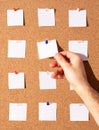 Vertical shot of a person's hand holding a blank paper note with tack on a notes board