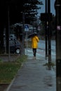 Vertical shot of a person in a yellow raincoat and umbrella walking on the sidewalk in Germany