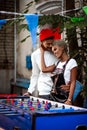 Vertical shot of pleasant looking mixed race female and her boyfriend embrace each other, stand near table football game Royalty Free Stock Photo