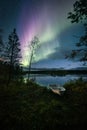 Vertical shot of the polar Aurora lights in the starry sky over the lake with a boat on a shore