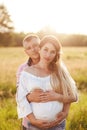 Vertical shot of pregant young woman with her lover stand closely, embrace, anticipate for child, stand together against green mea