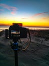 Vertical shot of a camera on a tripod placed on a shore and photographing the sunset at a beach Royalty Free Stock Photo