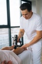 Vertical shot of professional male masseur massaging leg calf muscles using massage gun percussion tool of muscular Royalty Free Stock Photo