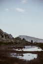 Vertical shot of a puddle reflecting a person climbing a mountain at San Vito Lo Capo, Italy