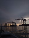 Vertical shot of the quay cranes silhouettes against the background of the cloudy sky at sunset.