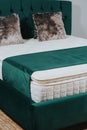 Vertical shot of a queen-size bed with green velvet headboard and fluffy cushions