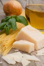 Vertical shot of raw spaghetti, parmesan, and basil on a wooden surface Royalty Free Stock Photo