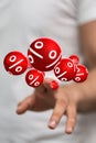 Vertical shot of red balls with white percentage signs behind a person's fingers