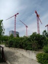 Vertical shot of red construction cranes surrounded by greenery under a cloudy sky at daytime