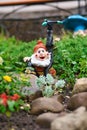 Vertical shot of a red-hatted garden dwarf placed next to a water sprinkler