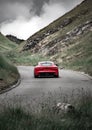 Vertical shot of a red supercar driving uphill through a valley on a cloudy day