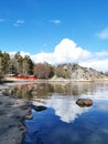 Vertical shot of reflective water near a beach with painted cabins, forest, and cloudy sky