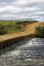 Vertical shot of a river flowing next to a country road under the white clear sky Royalty Free Stock Photo