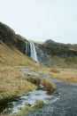 Vertical shot of a road in the field with a waterfall in the mountains in the background