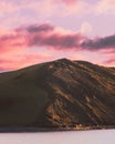 Vertical shot of the rocky hill by the sea under a pink sky with clouds Royalty Free Stock Photo