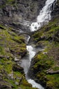 Vertical shot of the rocky mountains covered with grass with a small waterfall under a bridge Royalty Free Stock Photo