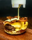 Vertical shot of sauce pouring on cheeseburger sandwich with fried bacon on wood Royalty Free Stock Photo