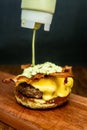 Vertical shot of sauce pouring on cheeseburger sandwich with fried bacon on wood Royalty Free Stock Photo