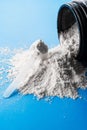 Vertical shot of a scoop of creatine powder on a scattered powder on a blue surface