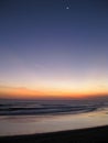 Vertical shot of the sea under a sky with a half moon during sunset Royalty Free Stock Photo