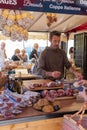 Vertical shot of seller in local market with various choice of dry hams wines and homemade products