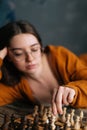 Vertical shot of serious sexy young woman making chess move lying on wooden vintage floor in dark room. Royalty Free Stock Photo