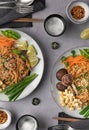 Vertical shot of servings of delicious noodles with salad, lime, greens, carrot, and crumbs