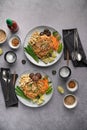 Vertical shot of servings of delicious noodles with salad, lime, greens, carrot, and crumbs