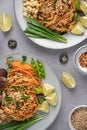 Vertical shot of servings of delicious noodles with salad, lime, greens, carrot, and crumbs