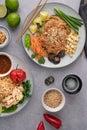 Vertical shot of servings of delicious noodles with salads, lime, greens, sauce, and crumbs