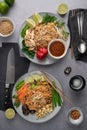 Vertical shot of servings of delicious noodles with salads, lime, greens, sauce, and peppers